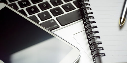Close up of smartphone, pen and notepad on a computer keyboard