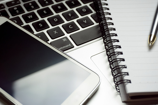 Close up of smartphone, pen and notepad on a computer keyboard