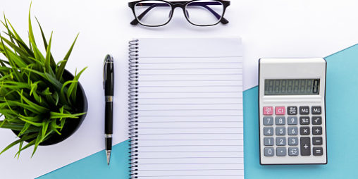 Top view of note pad, calculator, pen, eyeglasses and green plant