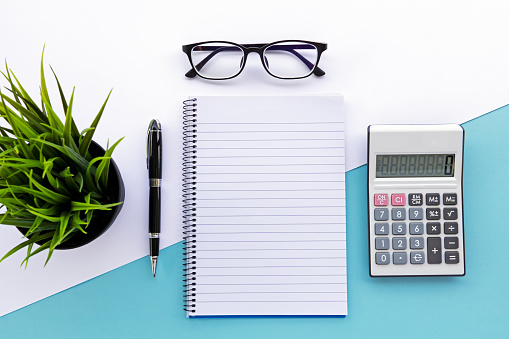 Top view of note pad, calculator, pen, eyeglasses and green plant